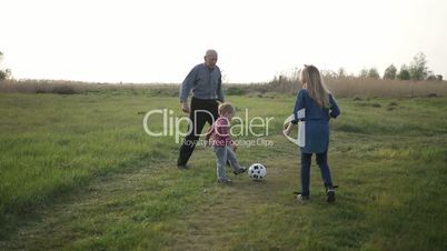 Toddler boy playing soccer with family outdoors