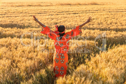 African woman in traditional clothes arms raised in field of cro