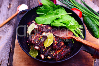 Pork ribs fried on a black cast-iron frying pan, meat marinated