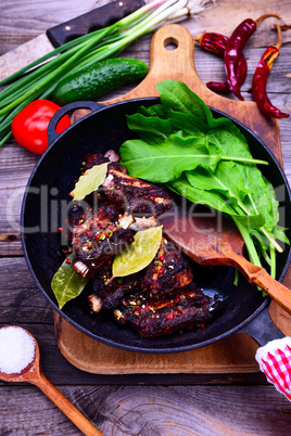 Cooked in spices pork ribs on a black cast-iron frying pan