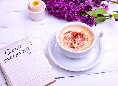 Cappuccino in a white cup, next note with the inscription good m