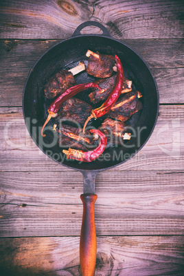 Pork ribs and hot pepper in a black frying pan with a handle