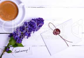 sealed letter on a white wooden surface, near a lilac bud and a