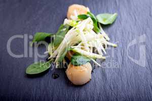 Scallop salad with apple, spinach on a stone plate.