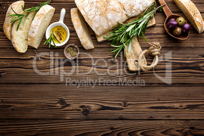 Delicious homemade italian ciabatta bread with olive oil and olives on wooden rustic background, above view