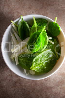 A Spinach Salad with apple on a stone surface.