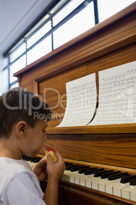 Close up of boy eating apple while sitting by piano