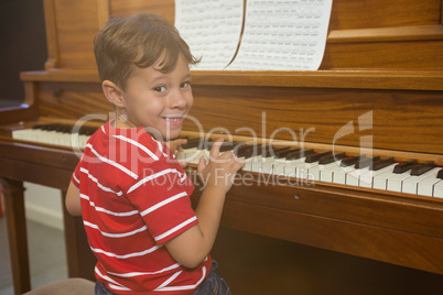Portrait of cheerful boy playing piano while sitting in classroom