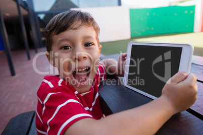 Portrait of cute boy holding digital tablet while sitting at table