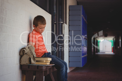 Sad boy sitting on bench by wall in corridor