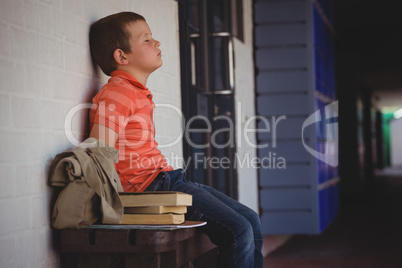 Sad boy with eyes closed sitting on bench by wall in corridor