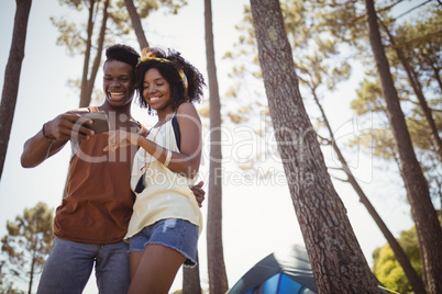 Happy couple using smart phone while standing by tent