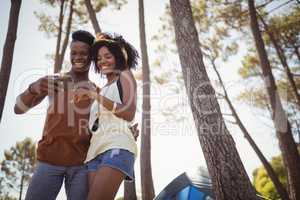 Happy couple using smart phone while standing by tent