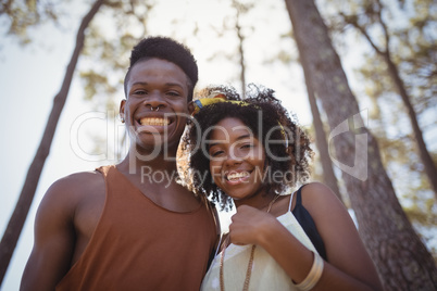 Low angle portrait of smiling couple standing against trees