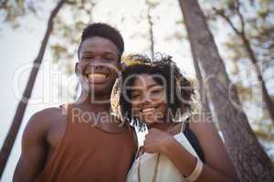 Low angle portrait of smiling couple standing against trees