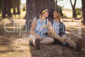 Couple sitting on field by tree trunk