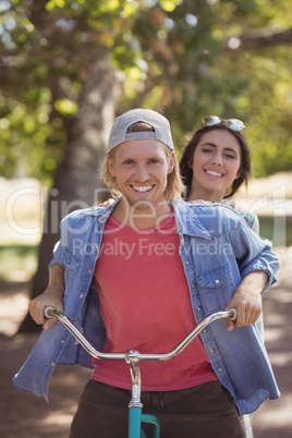 Portrait of smiling couple riding bicycle against trees