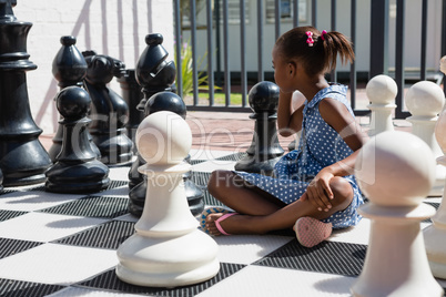 Side view of thoughtful girl sitting by chess pieces
