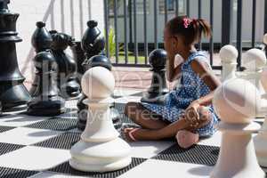 Side view of thoughtful girl sitting by chess pieces