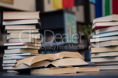 Stack of books on wooden table against shelf