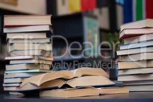 Stack of books on wooden table against shelf