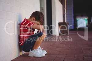 Side view of depressed boy crouching by wall
