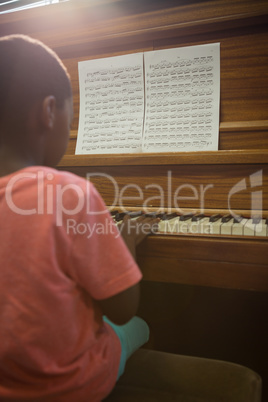 Rear view of boy practising piano in classroom