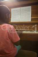 Rear view of boy practising piano in classroom