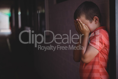 Boy covering his face with hands while standing in corridor