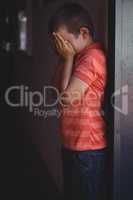 Side view of boy covering his face with hands while standing in corridor