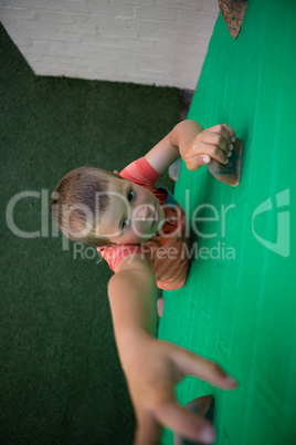 Boy reaching at climbing holds on green wall