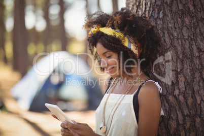Young woman using smart phone while standing by tree trunk