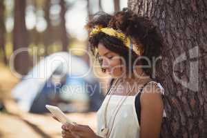 Young woman using smart phone while standing by tree trunk