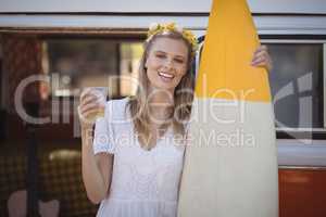 Portrait of woman holding beer glass and surfboard against van