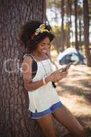 Smiling woman using mobile phone while standing against tree