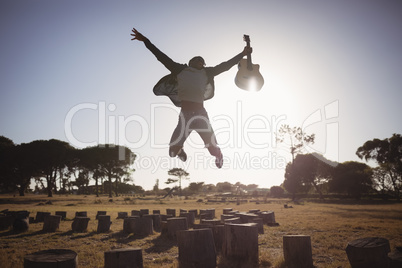 Happy man holding guitar while jumping against clear sky