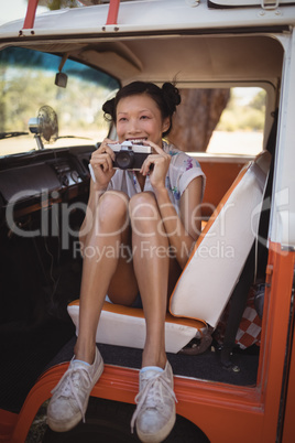Cheerful woman holding camera while sitting in motor home