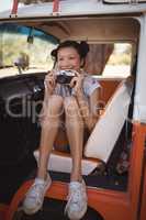 Cheerful woman holding camera while sitting in motor home