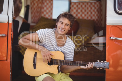Portrait of man playing guitar while sitting in van