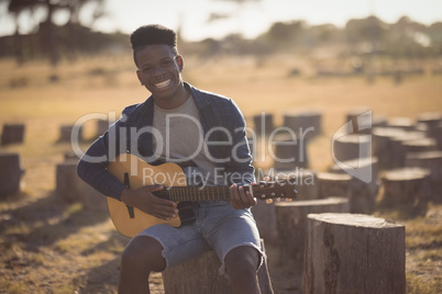 Portrait of smiling young man playing guitar while sitting in forest