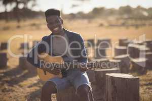 Portrait of smiling young man playing guitar while sitting in forest