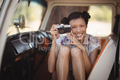 Portrait of smiling woman holding camera while sitting in van