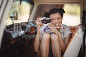 Portrait of smiling woman holding camera while sitting in van