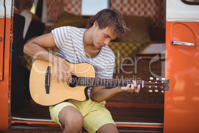 Young man playing guitar while sitting in motor home