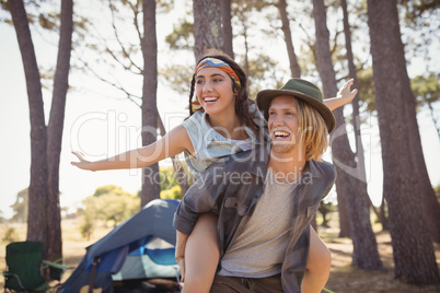 Cheerful man piggybacking  woman against trees