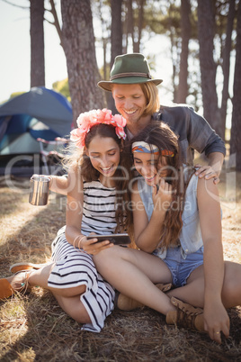 Happy friends using smart phone while sitting on field