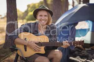 Portrait of smiling young man playing guitar while sitting on chair