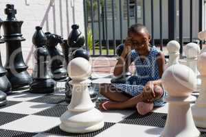 Thoughtful girl sitting by chess pieces