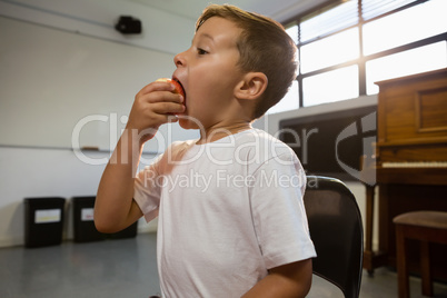 Close up of boy eating apple while standing against piano