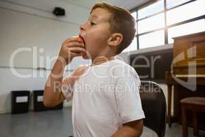 Close up of boy eating apple while standing against piano